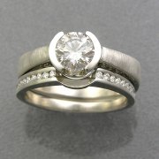 Engagement Ring 2-5: Round cut diamond partial bezel set in white gold with diamonds on the side shown with channel set diamond band