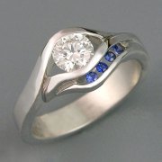 Engagement Ring 4-4: Round cut diamond partial bezel set in platinum with channel set blue sapphires