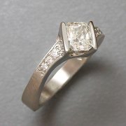 Engagement Ring 4-8: Radiant cut diamond channel set in white gold set at an angle with bead set diamonds on the sides