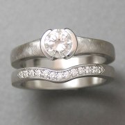 Engagement Ring 5-11: Round cut diamond partial bezel set in white gold shown with matching curved bead set diamond band