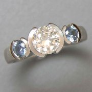 Engagement Ring 5-9: Round cut diamond partial bezel set in white gold with blue Montana sapphires on the sides