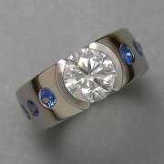 Engagement Ring 6-1: Round cut diamond partial bezel set in platinum with flush set blue sapphires on the sides