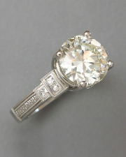 Engagement Ring 7-12: Round cut diamond prong set in platinum with diamonds and mill grain on the sides