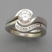 Engagement Ring 7-4: Round cut diamond partial bezel set in white gold shown with matching channel set diamond band