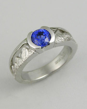 Engagement Ring 7-6: Round cut blue sapphire partial bezel set in platinum with mountains on the sides